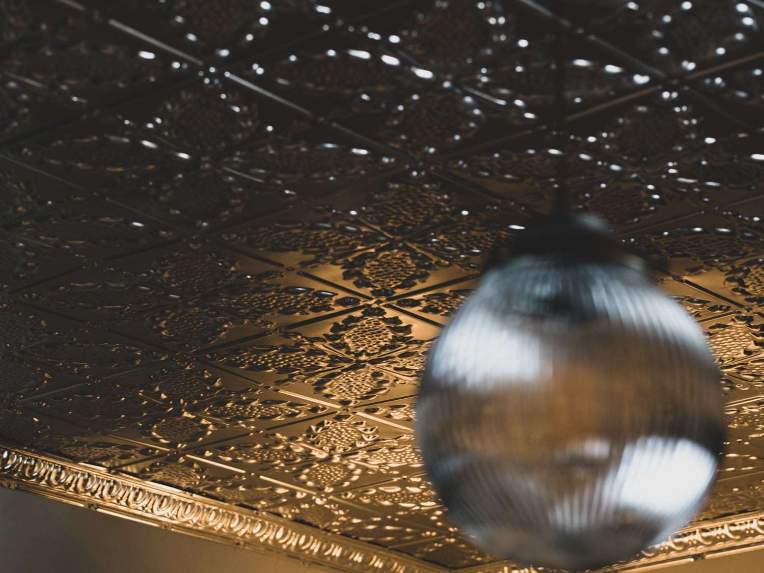 A detailed view of an ornate metal ceiling and a blurred pendant lamp in the foreground.