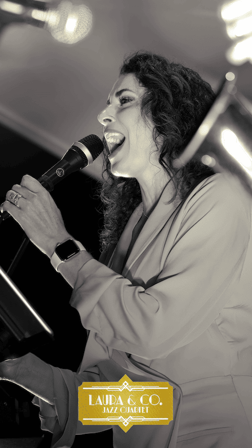 A black and white image of a female jazz singer performing on stage, holding a microphone, with a "Lauda & Co. Jazz Cabaret" sign visible.