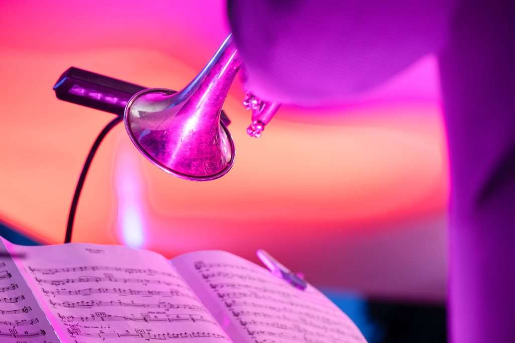 A trumpet resting near an open sheet music book with a colorful pink and purple background