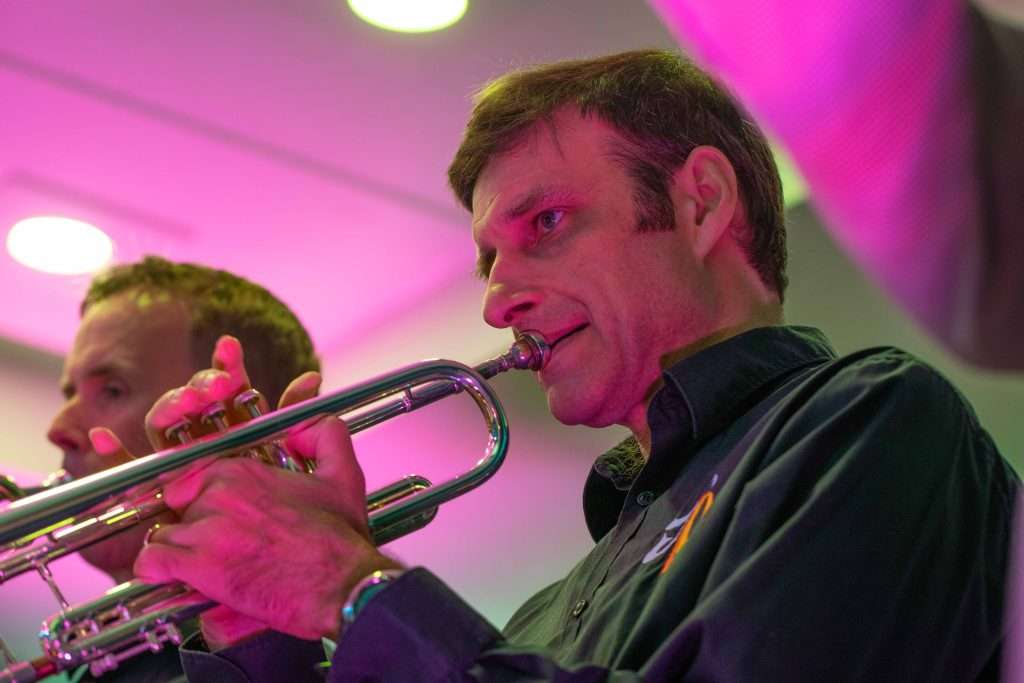 Two men playing trumpets on stage with purple lighting in the background.
