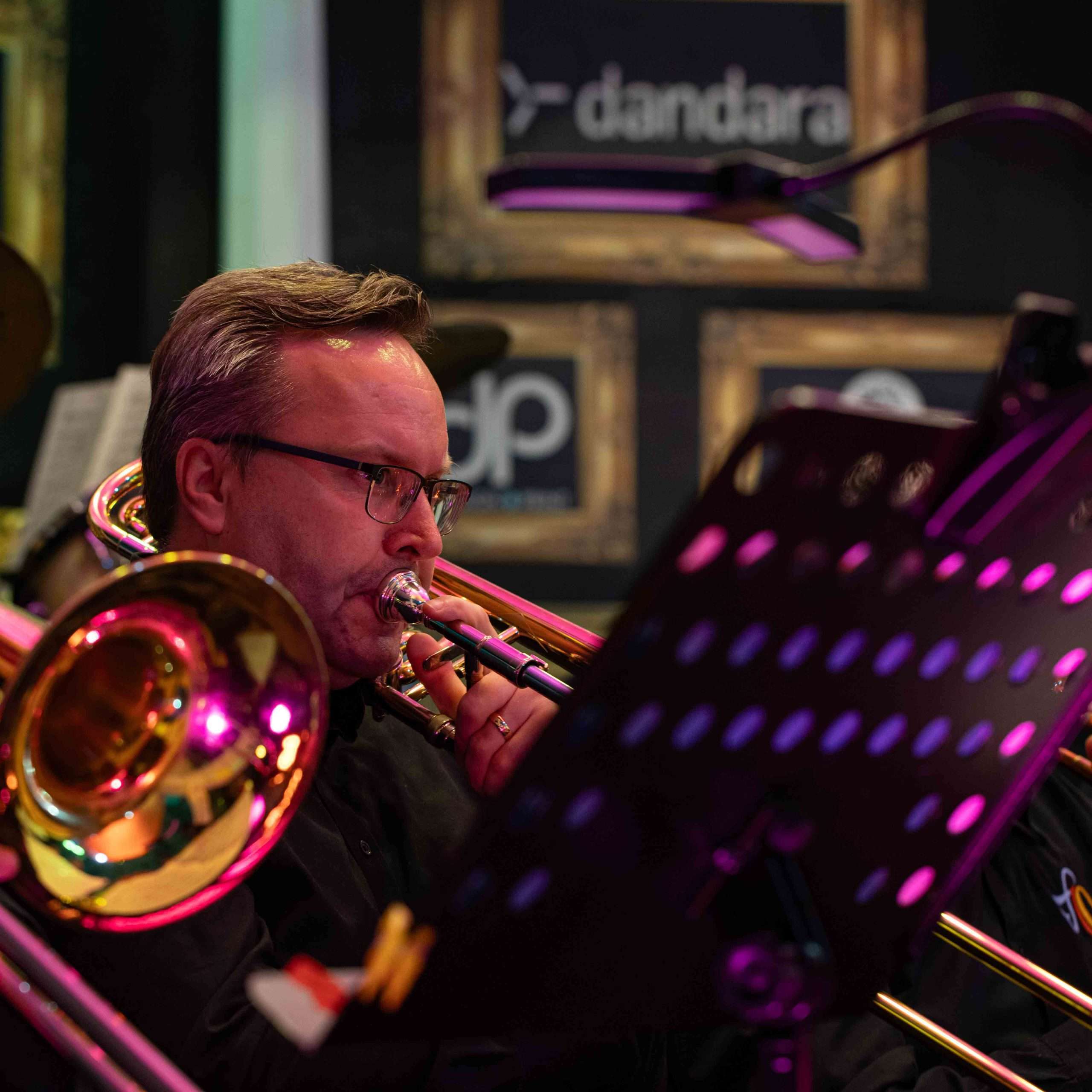 A musician playing the trombone during a live jazz performance with sheet music on a stand in front of him.