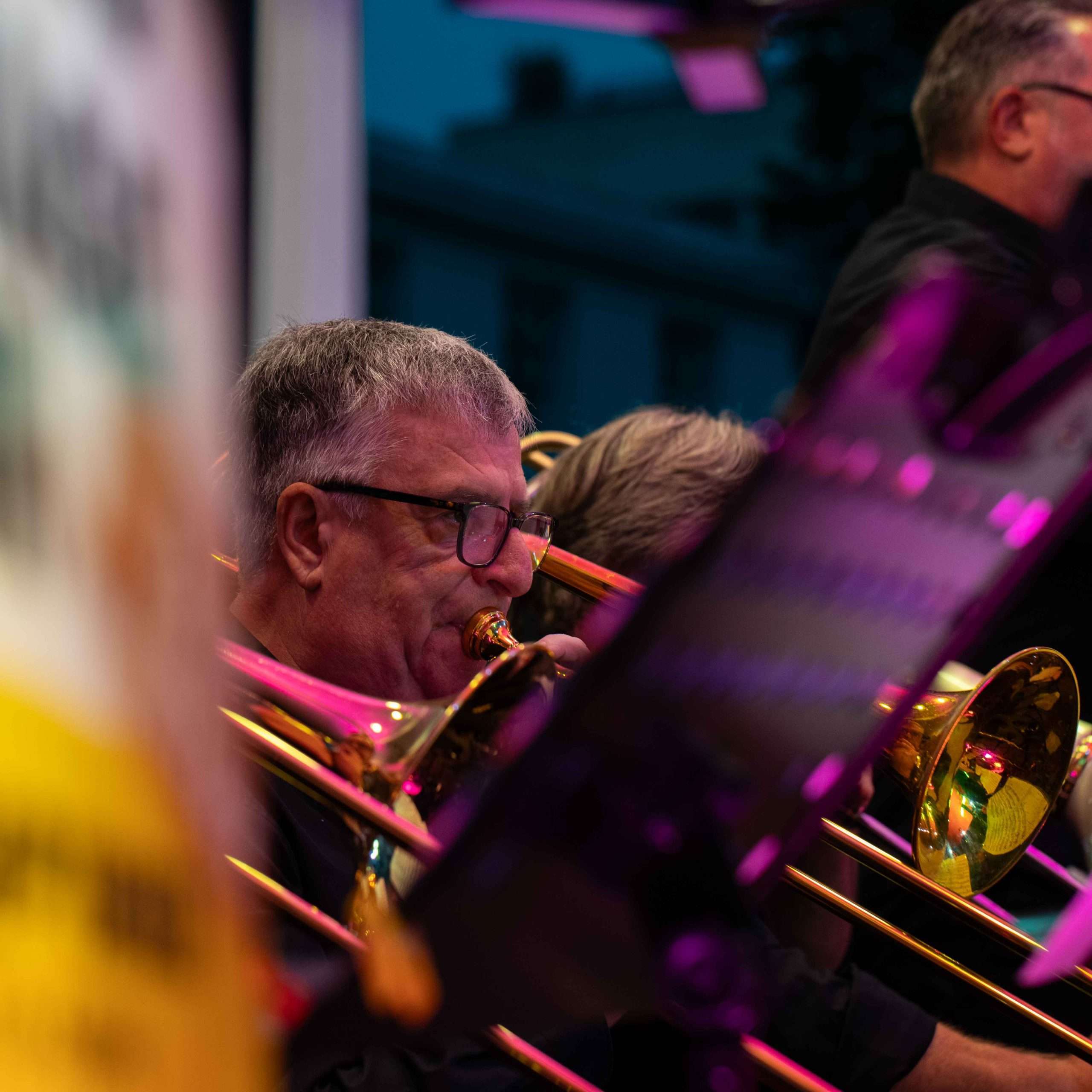 A trombone player performing in a brass ensemble, surrounded by vibrant colors and fellow musicians.