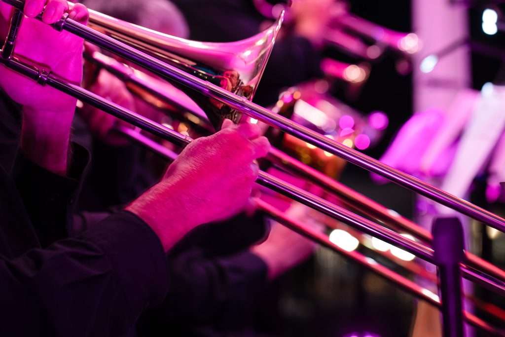 Close-up of a musician's hands playing the trombone with a blurred stage background.
