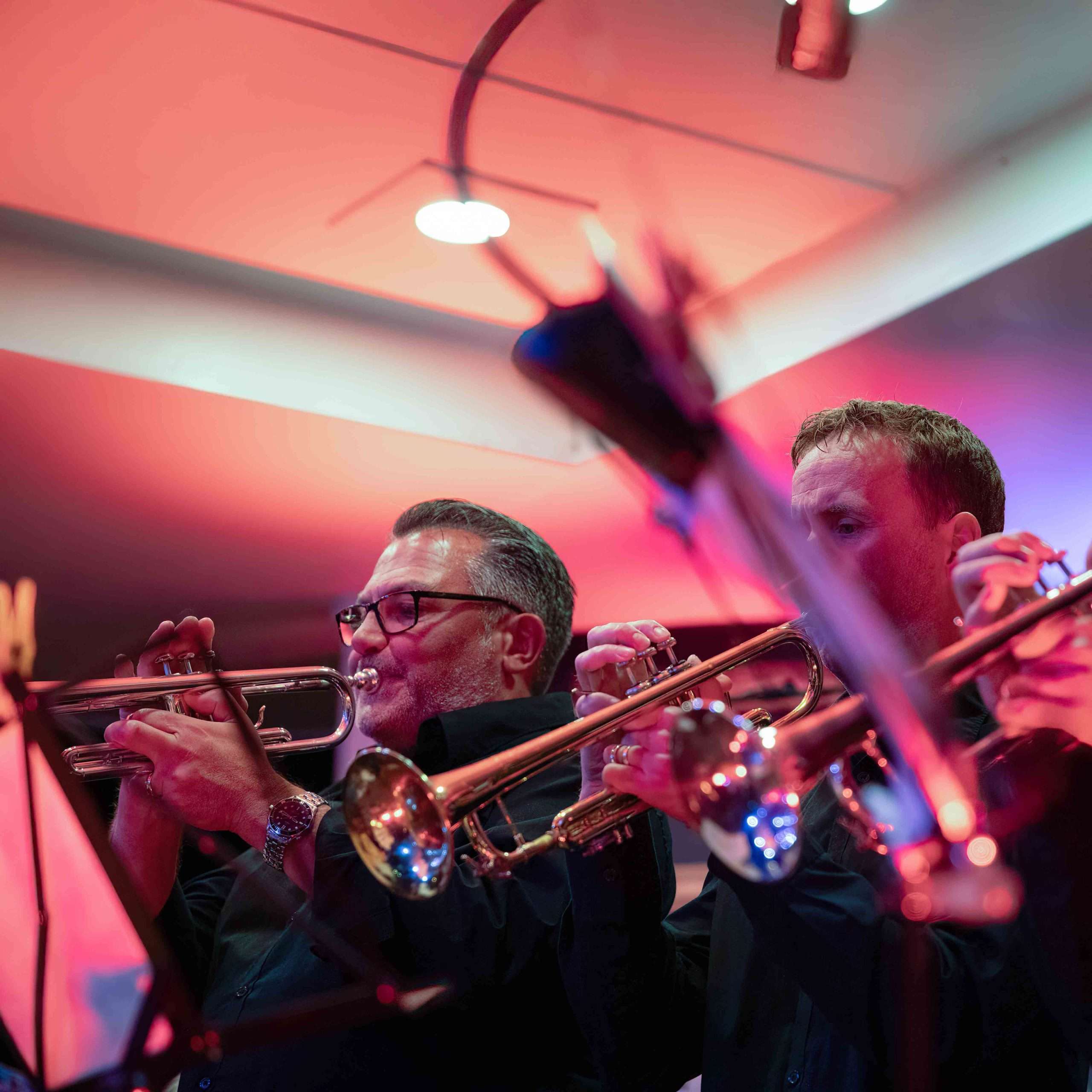 Two trumpet players performing on stage with a warm colored lighting backdrop.