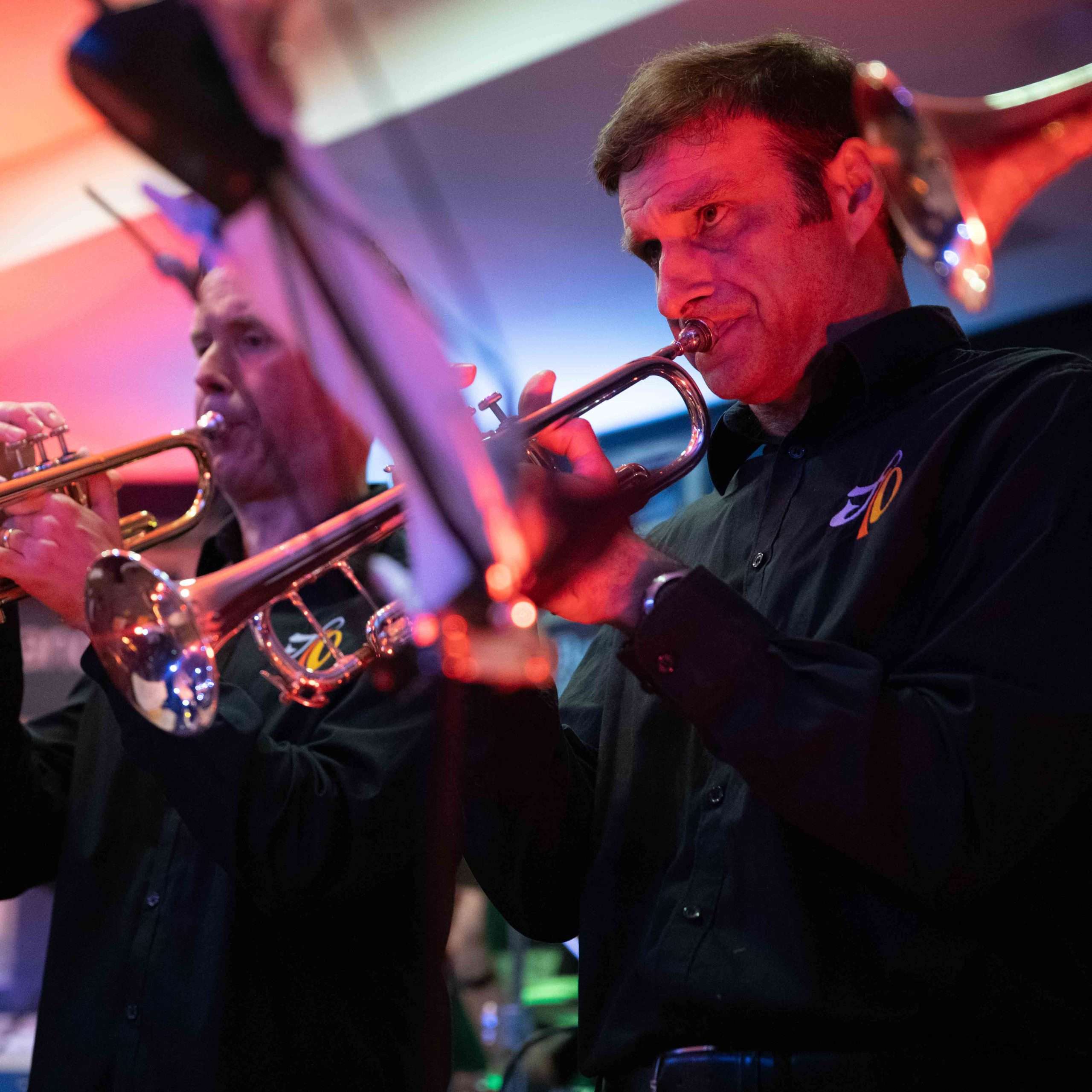 Two trumpeters playing their instruments in a live music setting with colorful stage lighting.
