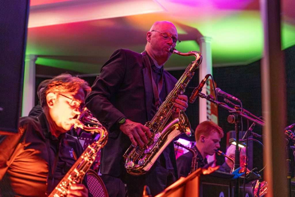 Two saxophonists performing on stage with colorful stage lighting in the background