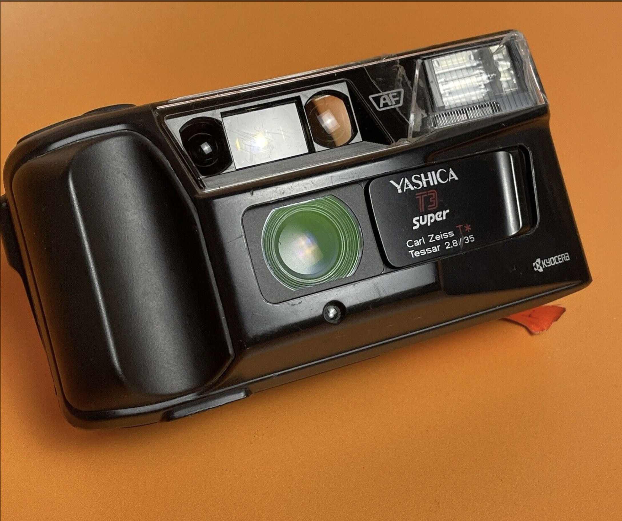 A Yashica T3 Super camera with Carl Zeiss Tessar lens on an orange background.
