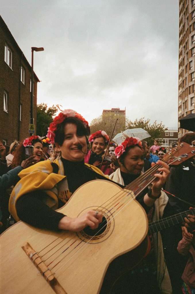 A group of smiling people with flower crowns playing guitars and enjoying a musical gathering outdoors.