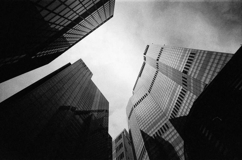 Black and white photograph looking up at towering skyscrapers converging against a cloudy sky