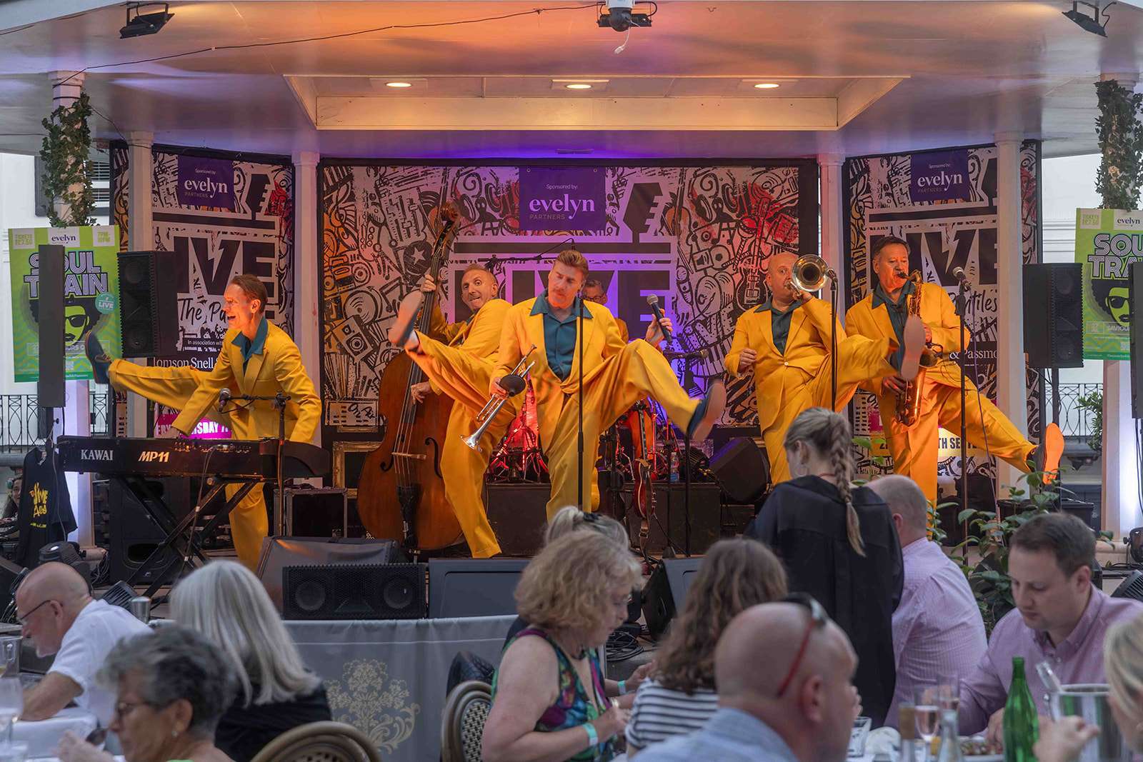 A lively jazz band performing on stage in matching yellow suits for an audience in a restaurant setting