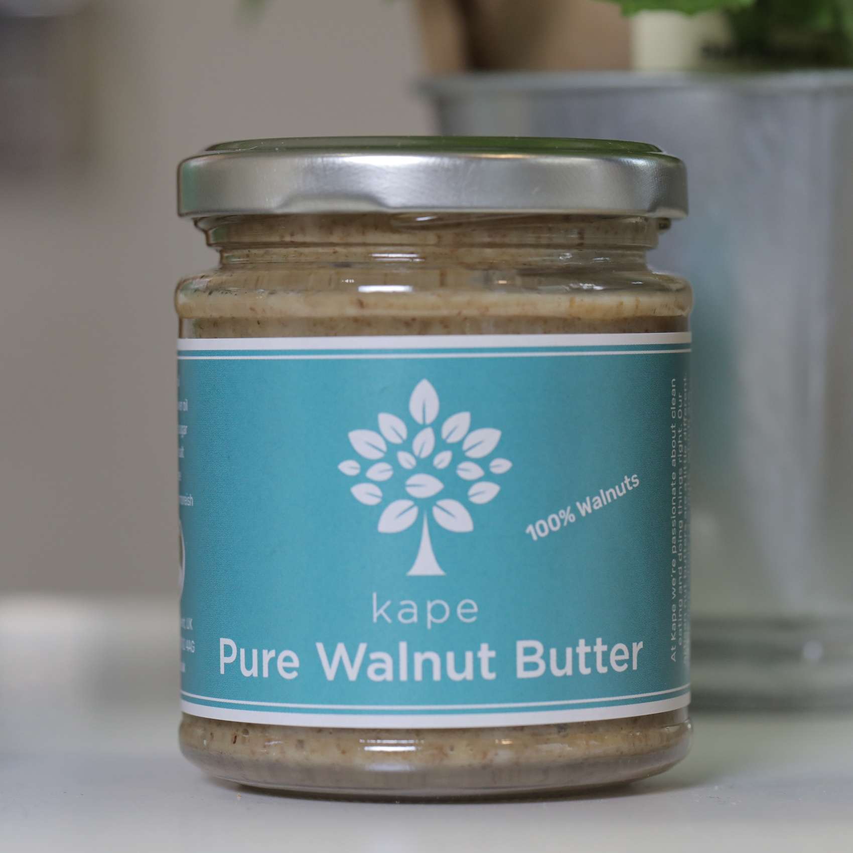 A glass jar of Kape brand pure walnut butter with a blue label, indicating 100% walnuts, on a kitchen counter.