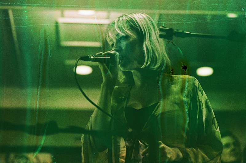 A female singer performing into a microphone with a moody, green lit ambiance.