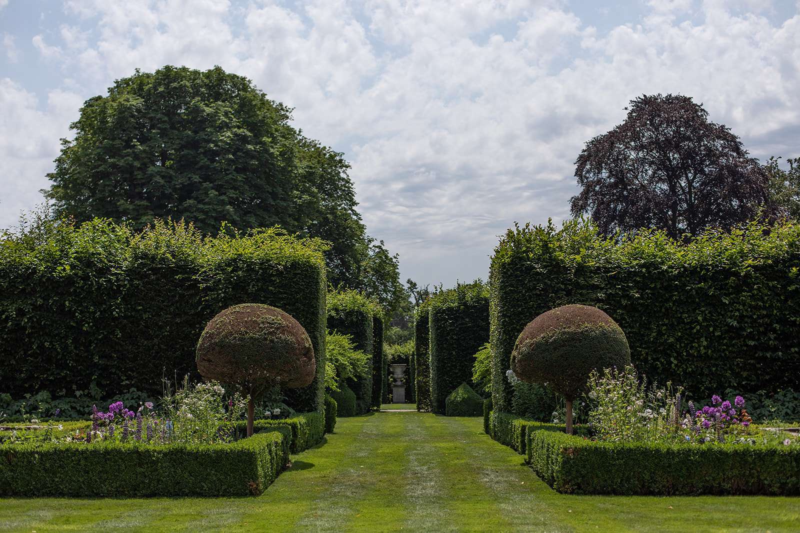 A well-manicured formal garden with topiary and hedges under a partly cloudy sky