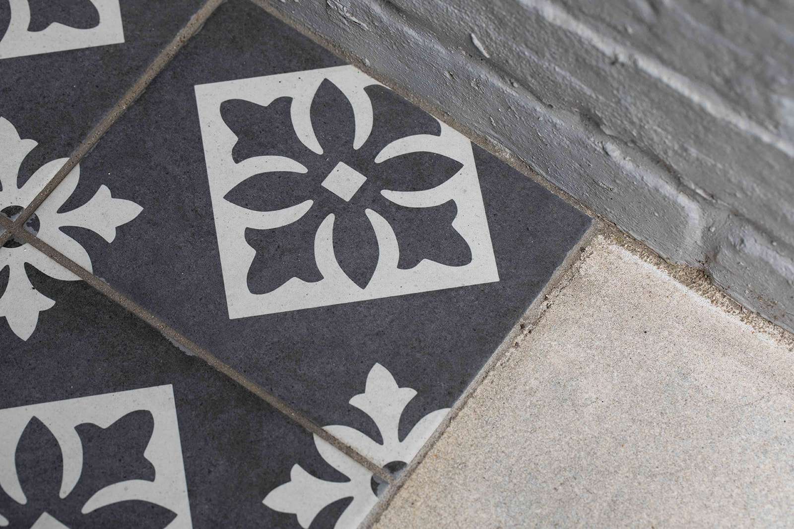Close-up view of decorative tile flooring with a floral design against a gray concrete background.