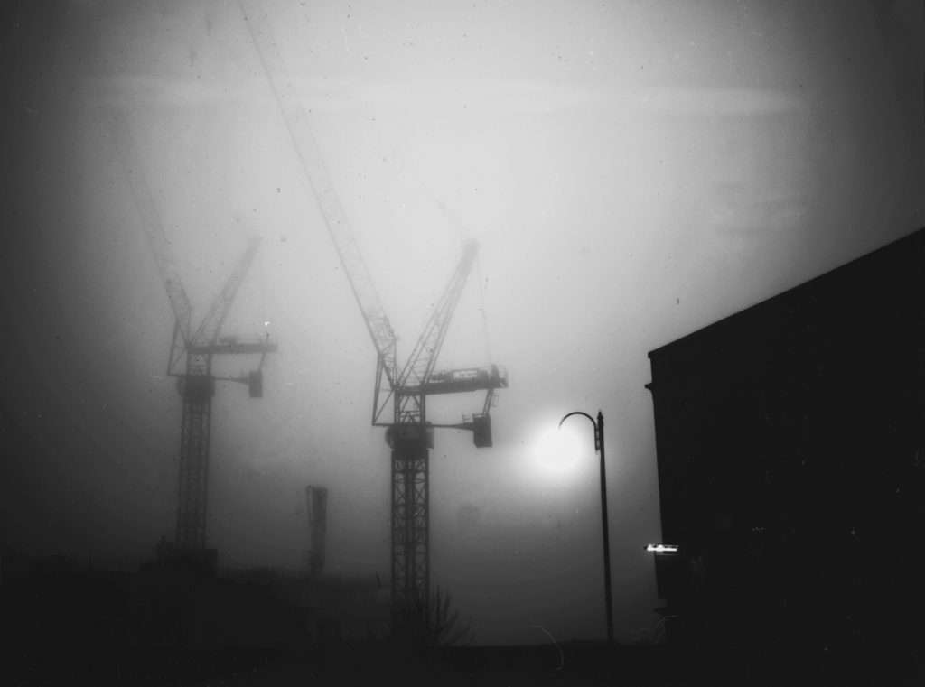 Misty view of 2 cranes with a building in the foreground in black and white